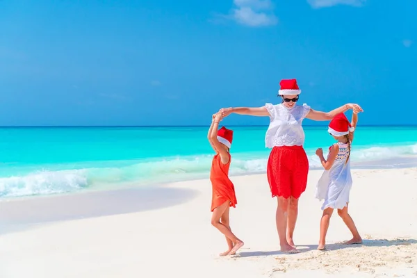 Happy beautiful family of mother and kids in red Santa hats on a tropical beach celebrating Christmas holiday — Stock Photo, Image