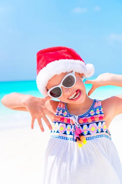 Fröhliche lustige kleine Mädchen mit Weihnachtsmütze während der Weihnachtsferien am Strand haben eine Menge Spaß — Stockfoto