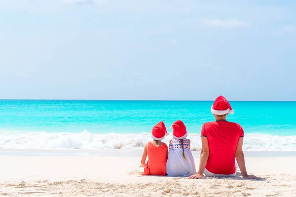 Feliz hermosa familia de padre e hijos en sombreros rojos de Santa en una playa tropical celebrando las vacaciones de Navidad —  Fotos de Stock