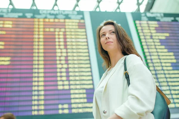 Jovem mulher no aeroporto internacional olhando para a placa de informações de voo verificando se há voo — Fotografia de Stock