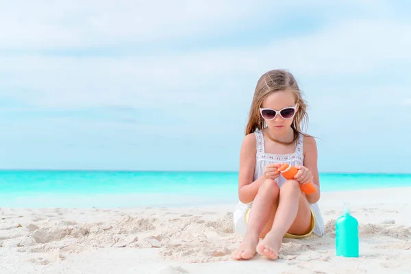 Niña adorable con botella de crema solar en la playa —  Fotos de Stock