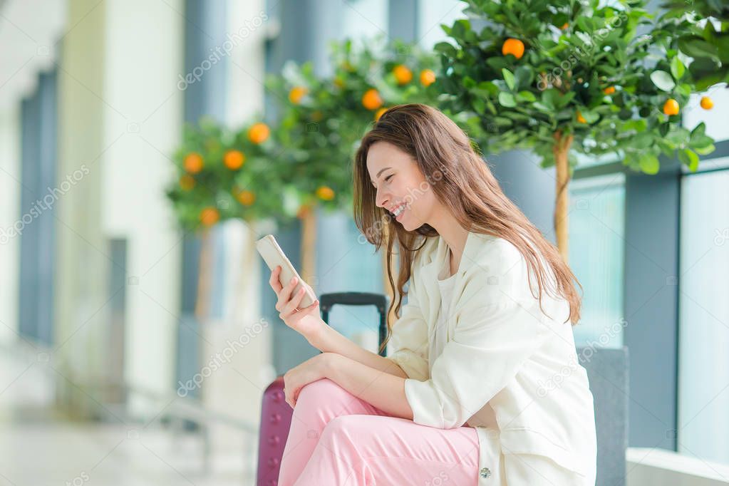 Young woman in international airport with her luggage and smartphone waiting for her flight