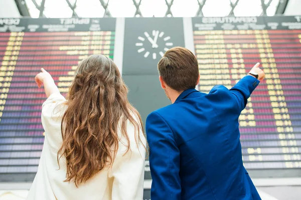 Молодые мужчина и женщина в международном аэропорту смотрят на табло информации о рейсах — стоковое фото