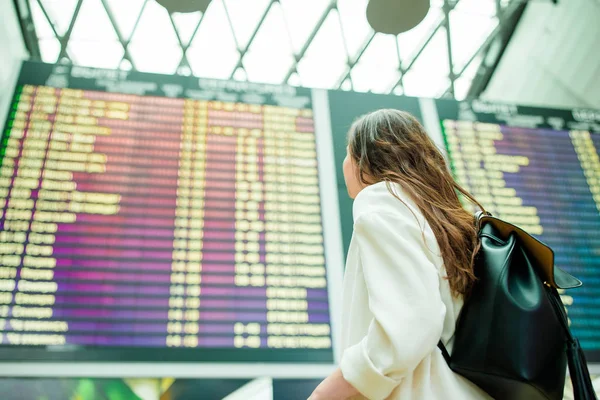 Vista trasera de la mujer en el aeropuerto internacional mirando la información de vuelo tablero de verificación de vuelo —  Fotos de Stock