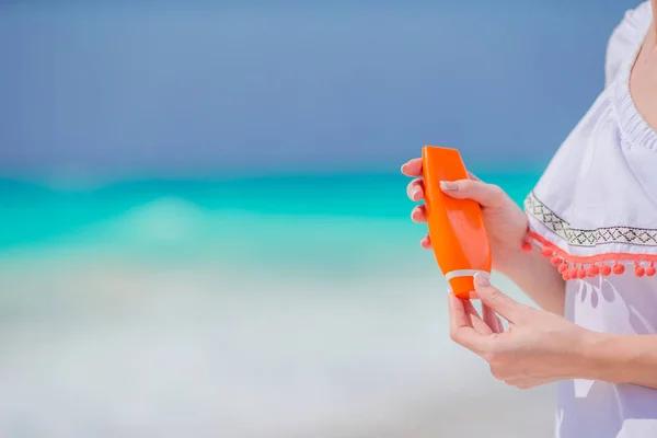 Botella de crema solar en manos femeninas en la playa . — Foto de Stock