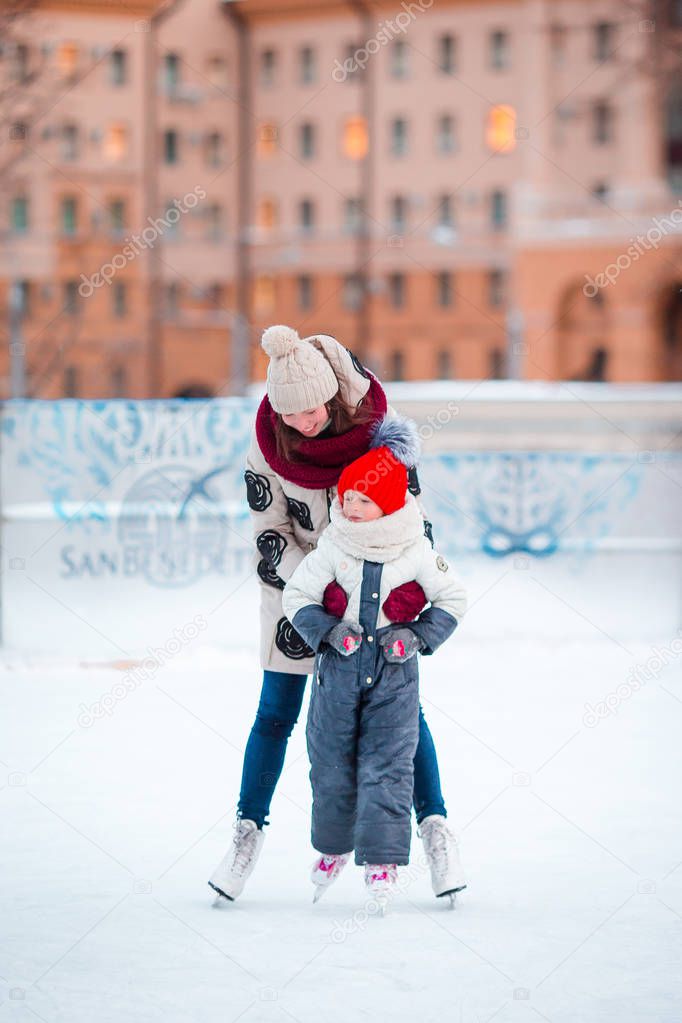 Little adorable girl with her mom skating on ice-rink