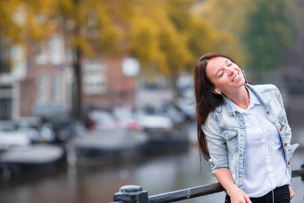 Ung vacker kvinna lyssna musik bakgrund av kanal i Amsterdam, Nederländerna — Stockfoto