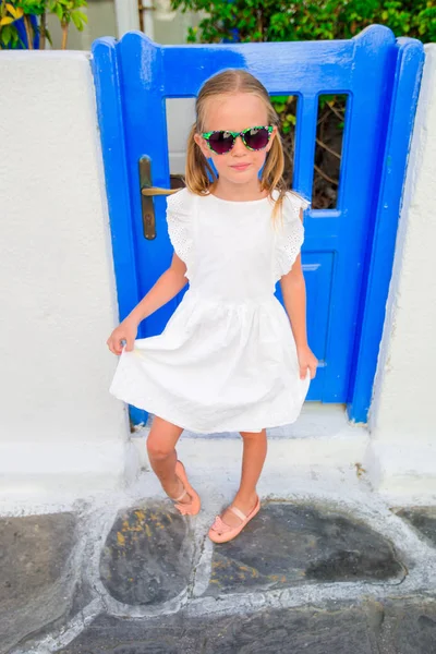 Kleine meisje portret buitenshuis in oude Grieks dorp. Kid op straat van Grieks dorp met witte wanden en kleurrijke deuren — Stockfoto