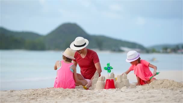 Vader en kleine kinderen maken zandkasteel op tropisch strand — Stockvideo