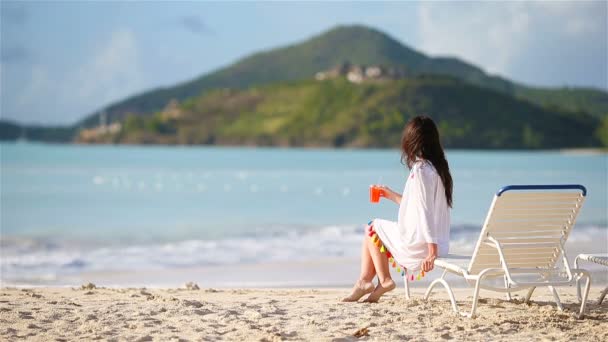 Mladá žena s koktejlovým sklem na bílé pláži sedí na soláriu — Stock video