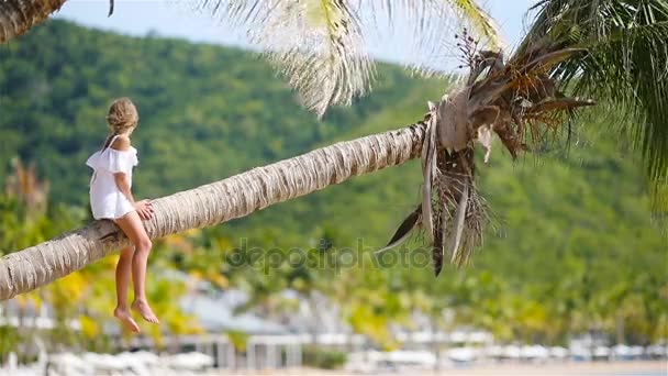 Вид на очаровательную маленькую девочку на тропическом пляже, сидящую на пальме во время летних каникул — стоковое видео