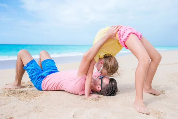 Padre y niña en la playa divirtiéndose mucho. Deportivo niño hace ejercicios deportivos en la orilla del mar —  Fotos de Stock
