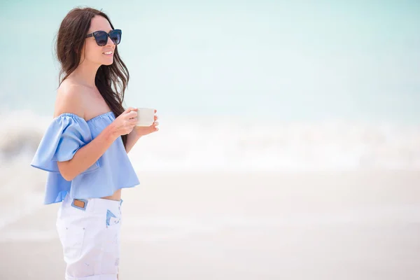 Mujer joven con café caliente disfrutando de vista a la playa . — Foto de Stock