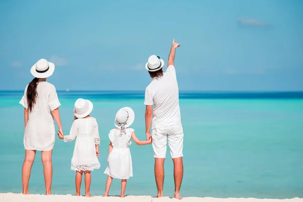 Joven familia de cuatro en blanco en la playa tropical. PArent con dos niños pequeños mirando al mar — Foto de Stock