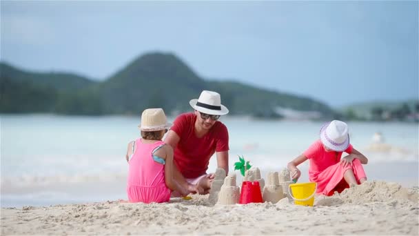 Familia haciendo castillo de arena en la playa tropical blanca. Padre y dos niñas jugando con arena en la playa tropical — Vídeo de stock