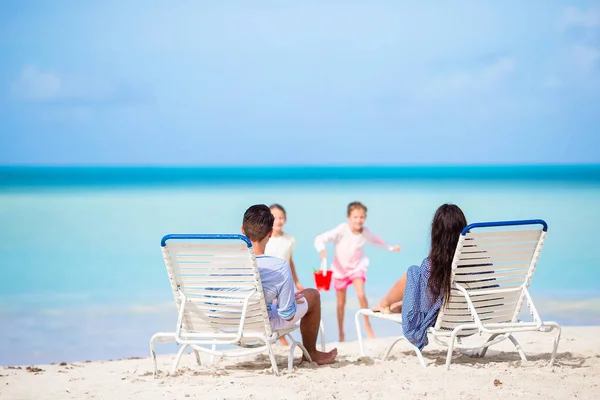 Feliz hermosa familia de cuatro en la playa. Los padres se relajan en la tumbona y los niños se divierten en la costa — Foto de Stock