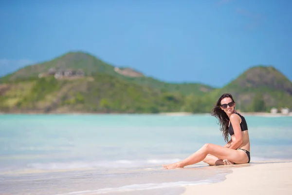 En kvinne sitter på stranden og ler og nyter sommerferien og ser inn i kameraet. Vakker modell i bikini sittende . – stockfoto