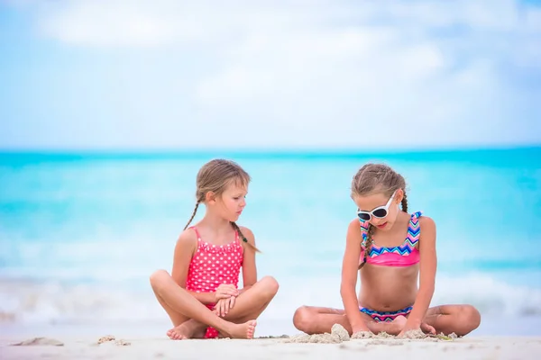 Imádnivaló kislányok játszanak homokkal a parton. Gyerekek ülnek a sekély vízben és homokvárat építenek. — Stock Fotó