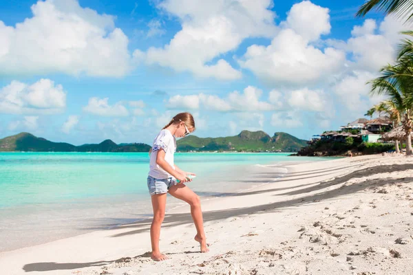 Очаровательная маленькая девочка на тропическом пляже наносит крем от загара — стоковое фото