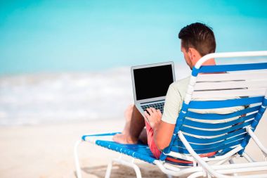 Tropikal Karayipler beach laptop olan genç adam. Şezlong bilgisayar ile oturup ve sahilde çalışma adam