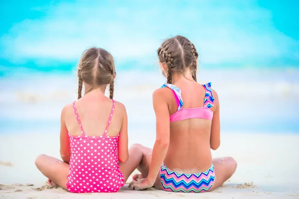 Adorable little girls playing with sand on the beach. Back view of kids sitting in shallow water and making a sandcastle — Stock Photo, Image