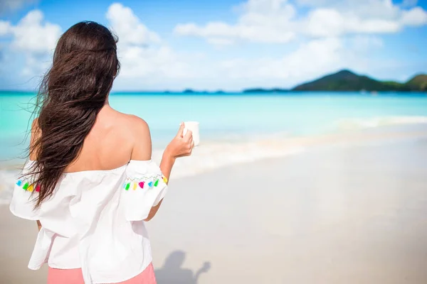 Молодая женщина с горячим кофе наслаждается видом на пляж . — стоковое фото