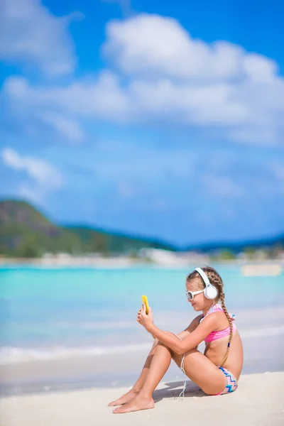 Little girl listening to music on headphones on the beach. Adorable kid enjoy music on the seashore — Stock Photo, Image