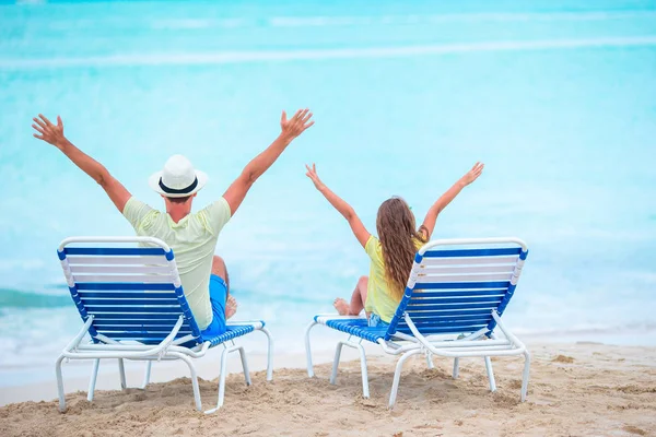 Padre e hija manos arriba en la playa sentados en chaise-longue —  Fotos de Stock