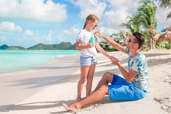 Joven padre aplicando crema solar a la nariz de la hija en la playa. Protección solar —  Fotos de Stock