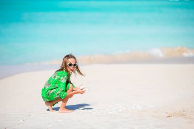 Little cute girl with seashell in hands at tropical beach. Adorable little girl playing with seashells on beach clipart