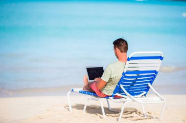 Tropikal Karayipler beach laptop olan genç adam. Şezlong bilgisayar ile oturup ve sahilde çalışma adam