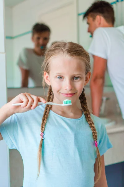 Niña hermosa con dientes blancos y su joven padre cepillándose los dientes en el baño — Foto de Stock