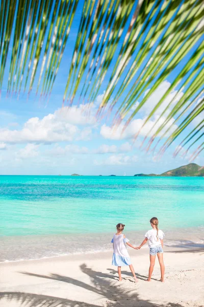 Vista trasera de las niñas en la playa de arena. Niños felices bajo la palmera en la playa tropical — Foto de Stock