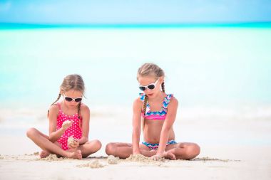 İki küçük mutlu kız, tropikal sahilde kumla oynarken çok eğleniyor.