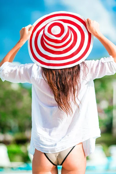 Mulher bonita jovem relaxante na beira da piscina infiniti. Visão traseira da menina em biquíni e chapéu vermelho grande — Fotografia de Stock