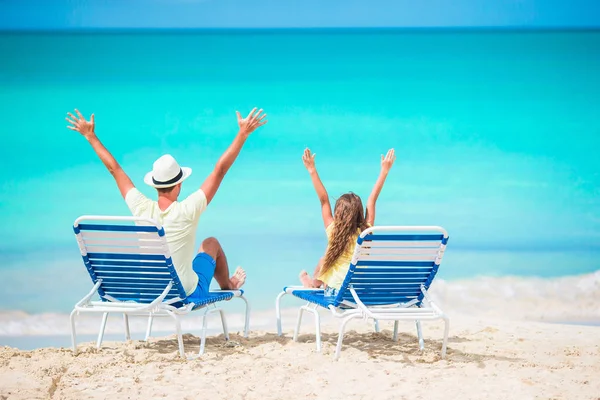 Padre e hija manos arriba en la playa sentados en chaise-longue —  Fotos de Stock