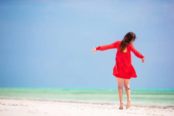 Νεαρή όμορφη γυναίκα στο κόκκινο φόρεμα διασκέδαση στον τροπικό αιγιαλού. Ευτυχισμένος κορίτσι περπάτημα σε τροπική παραλία με λευκή άμμο — Φωτογραφία Αρχείου