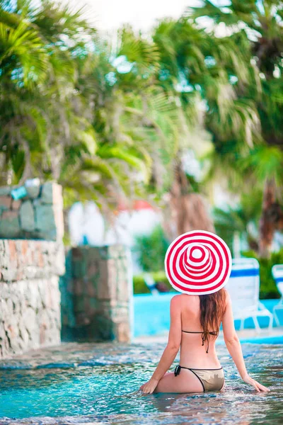 Jovem mulher bonita em grande chapéu vermelho desfrutando de férias de verão na piscina tranquila — Fotografia de Stock