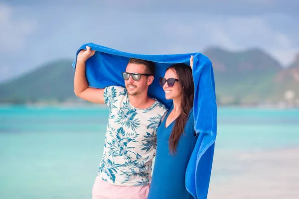 Pareja joven en la playa tropical bajo la toalla escondida de las lluvias tropicales. Concepto de viaje — Foto de Stock