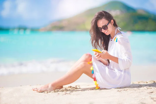 Młoda kobieta ze smartfonem podczas tropikalnych wakacji na plaży. Piękna dziewczyna na plaży z komórką na karaibskiej wyspie — Zdjęcie stockowe