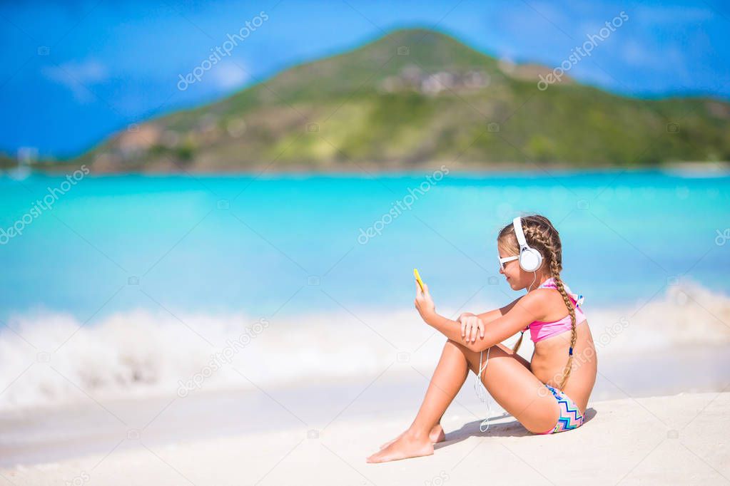 Little girl listening to music on headphones on caribbean beach