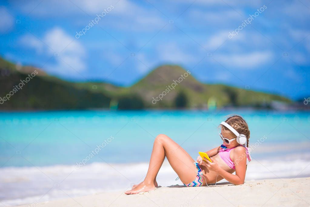 Little girl listening to music on headphones on caribbean beach