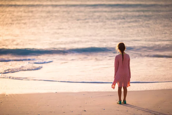 Αξιολάτρευτο ευτυχισμένη κοριτσάκι περπάτημα στην παραλία με λευκή στο ηλιοβασίλεμα. — Φωτογραφία Αρχείου