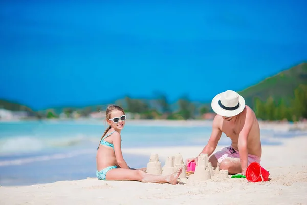 家族熱帯白いビーチで作る砂の城。父と熱帯のビーチに砂と遊ぶ女の子 — ストック写真