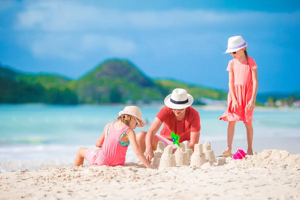 Family making sand castle at tropical white beach. Father and two girls playing with sand on tropical beach — Stock Photo, Image