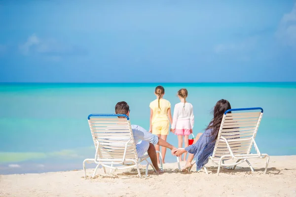 Ευτυχής όμορφη τετραμελής οικογένεια στην παραλία. Οι γονείς να χαλαρώνεις στην ξαπλώστρα και τα παιδιά διασκεδάζουν στην ακτή — Φωτογραφία Αρχείου
