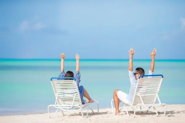 Two happy people having fun on the beach, sitting on comfortable sunbed with raised up hands for joy — Stock Photo, Image