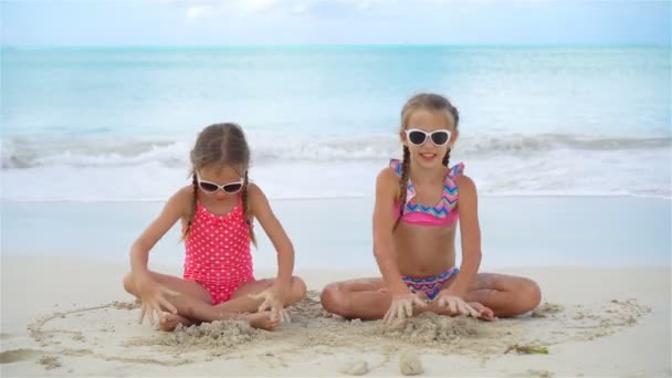 Очаровательные маленькие девочки играют с песком на пляже. Дети сидят на мелководье и строят песчаный замок — стоковое видео