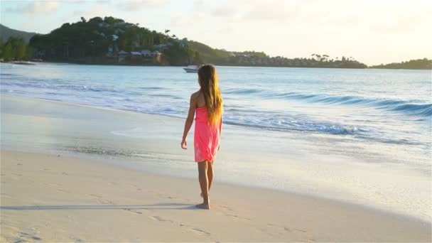 Αξιολάτρευτο ευτυχισμένη κοριτσάκι περπάτημα στην παραλία με λευκή κατά το ηλιοβασίλεμα. Βίντεο αργής κίνησης — Αρχείο Βίντεο