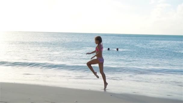 Kleines aktives Mädchen, das Wagenräder am Strand bei Sonnenuntergang macht. Zeitlupe — Stockvideo
